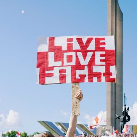 protester in Belarus holding sign reading "live, love, fight" in red and white
