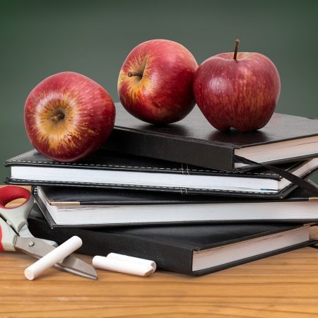 apples on top of a pile of books in front of chalkboard